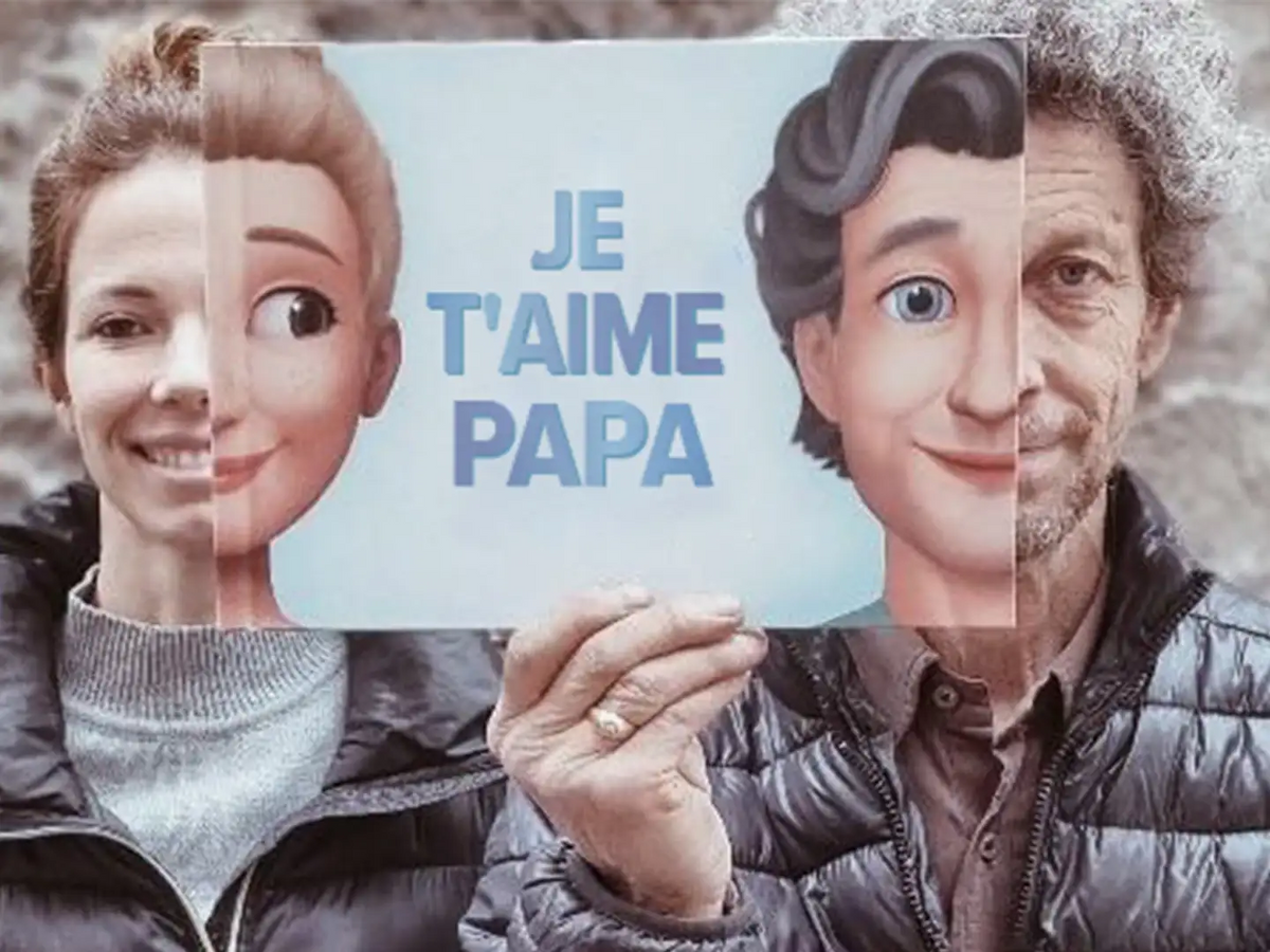 Un Papa et sa fille en train de jouer avec la couverture du livre pour papa, sur laquelle il apparaît avec son enfant adulte. La ressemblance est saisisante.