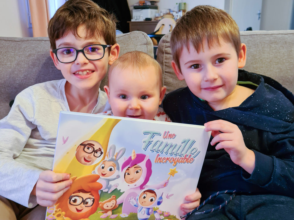 Trois enfants, dont un bébé, avec leur livre personnalisé pour les familles livré avec sa pochette.