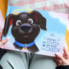 Gros plan sur un livre souvenir personnalisé pour chien intitulé « Hugo, un toutou qui avait du chien », avec un chien illustré et des ailes d’ange.