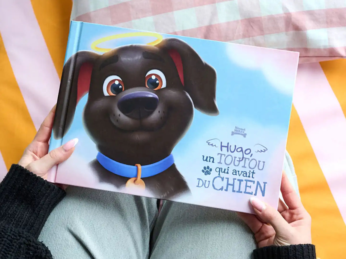 Gros plan sur un livre souvenir personnalisé pour chien intitulé « Hugo, un toutou qui avait du chien », avec un chien illustré et des ailes d’ange.
