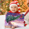 Bébé souriant en bonnet de Noël tenant le livre personnalisé “Notre Premier Noël 2025” avec Augustin et Maman.