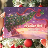 Livre de Noël personnalisé “Notre Premier Noël 2025” avec Anne et Papa, présenté devant un sapin décoré.